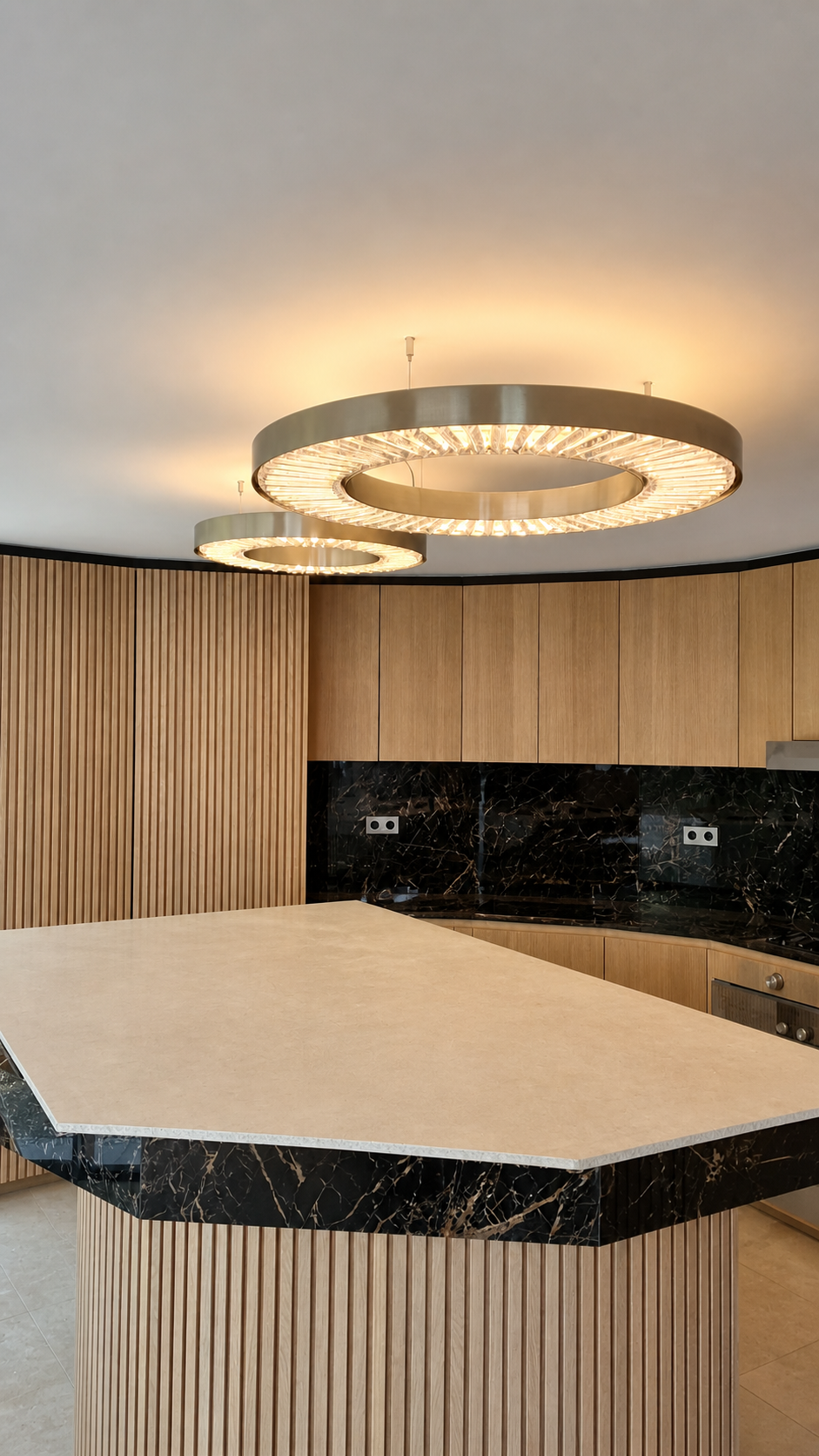 Cuisine de villa à Cannes réalisée par Aktive : îlot en chêne cannelé, plan en pierre claire, crédence en marbre noir, suspensions LED