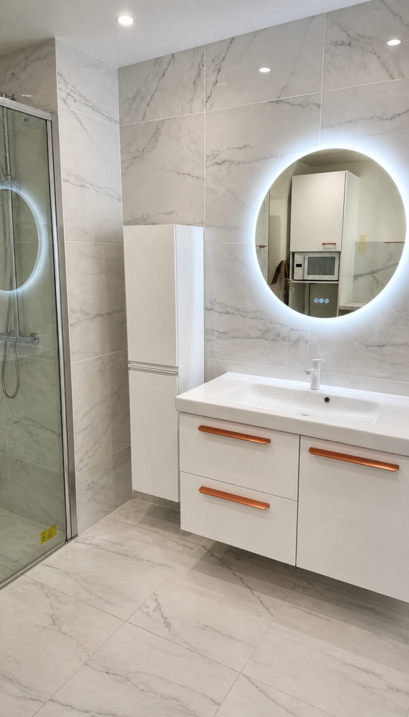 Salle de bain rénovée par Aktive à Grasse : carrelage effet marbre blanc, miroir rond rétroéclairé, meuble vasque suspendu