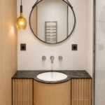 Salle de bain de villa à Saint-Jean-Cap-Ferrat réalisée par Aktive : meuble vasque cintré en chêne, plan en marbre noir, miroir rond, suspension ambrée
