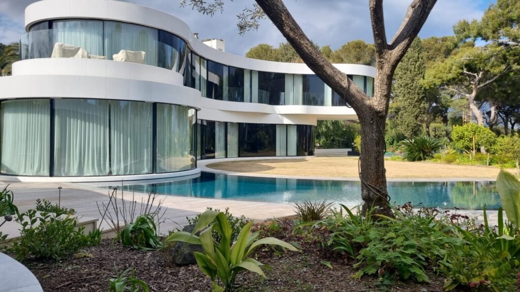 Villa de prestige à Antibes : façade courbe, terrasse en bois et piscine à débordement, vue depuis le jardin