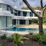 Villa de prestige à Antibes : façade courbe, terrasse en bois et piscine à débordement, vue depuis le jardin